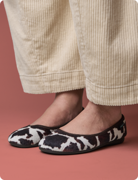 Black and white patterned shoes worn with beige pants on a red background