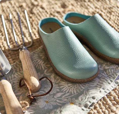 Pair of light blue clogs on a textured surface with gardening tools nearby.
