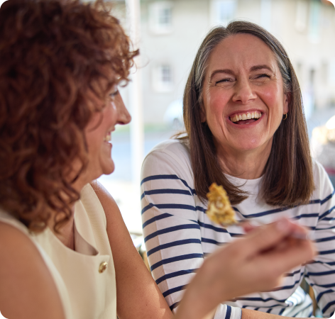 Two women laughing together, one with curly hair and the other with straight hair in a striped shirt.