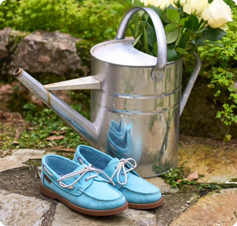 Blue shoes next to a silver watering can with flowers in the background