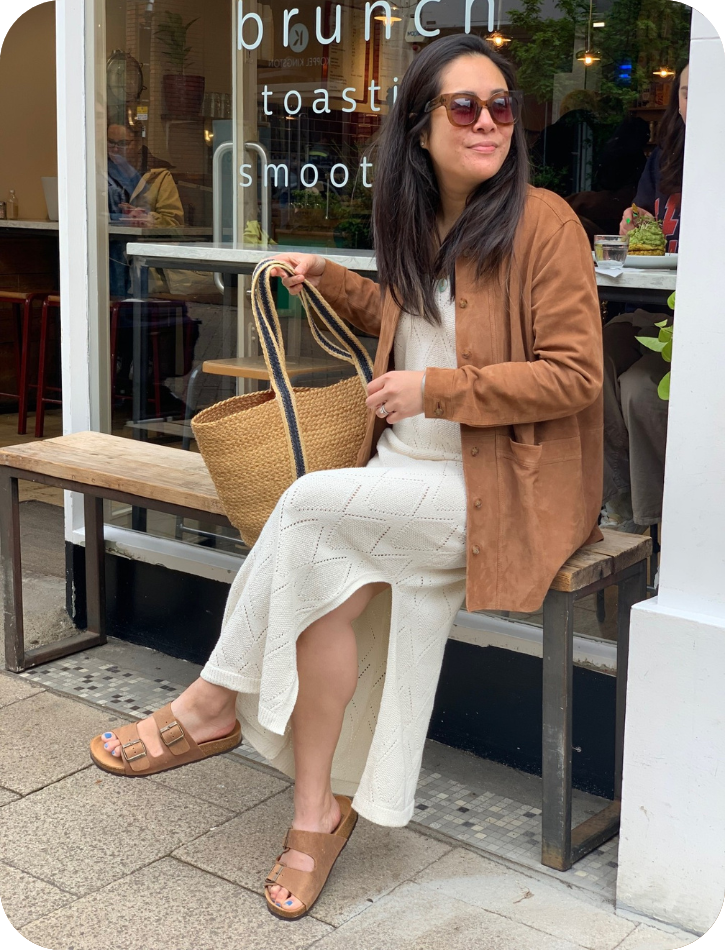 Woman sitting on a bench outside a cafe, holding a bag.