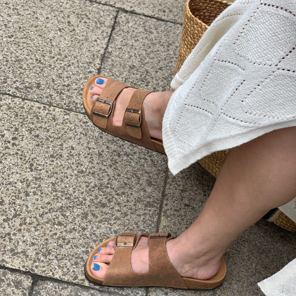 Person wearing brown sandals on a stone pavement