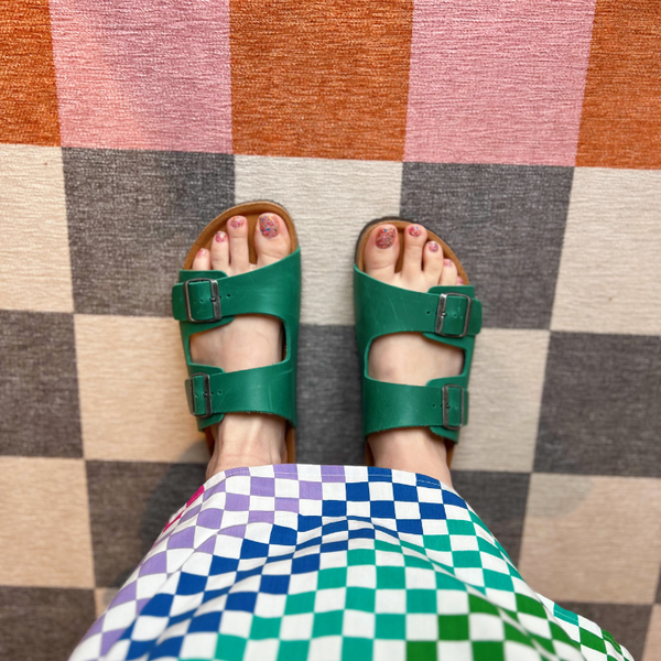 Green sandals on a checkered floor with colorful fabric.